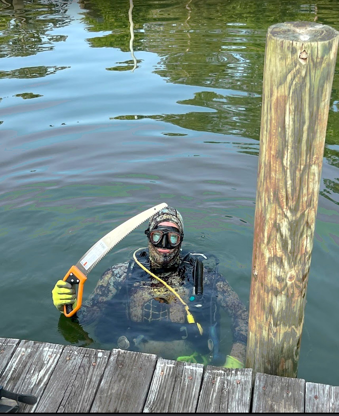 Phil at the surface in dive gear, holding a pruning saw next to a dock piling on Lake Norman